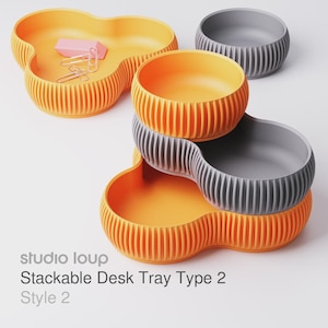 Pode incluir: Bandejas de mesa empilháveis ​​laranja e cinza com design canelado. Uma bandeja contém clipes de papel e uma borracha rosa. O texto "studio loup Stackable Desk Tray Type 2 Style 2" é visível.