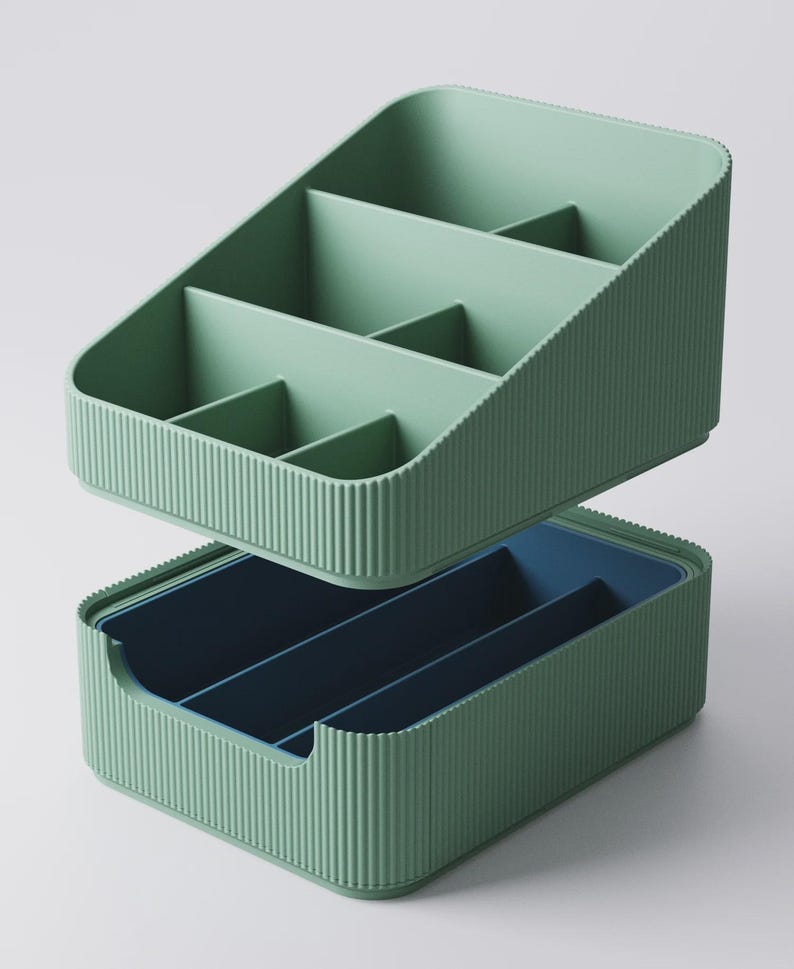 May include: Two-piece organizer set in a muted green color. The top section has multiple compartments, while the bottom section is a darker blue. Both pieces have a ribbed texture on the exterior, providing a modern aesthetic. Ideal for desk or vanity organization.