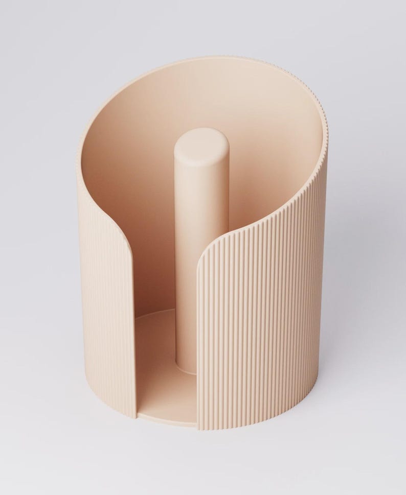 May include: A light peach-colored, cylindrical paper towel holder. The holder has a vertical, central post and a curved, ridged exterior. The design is minimalist and modern, suitable for kitchen or bathroom decor.