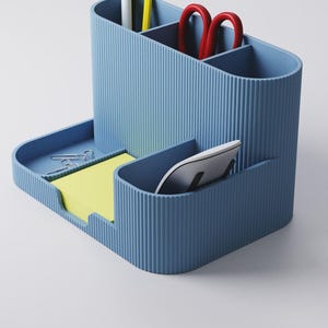 May include: A blue desk tidy with several sections. It contains a pen, pencil, and red scissors. A tray holds paper clips and yellow sticky notes. A white computer mouse is in a separate compartment.