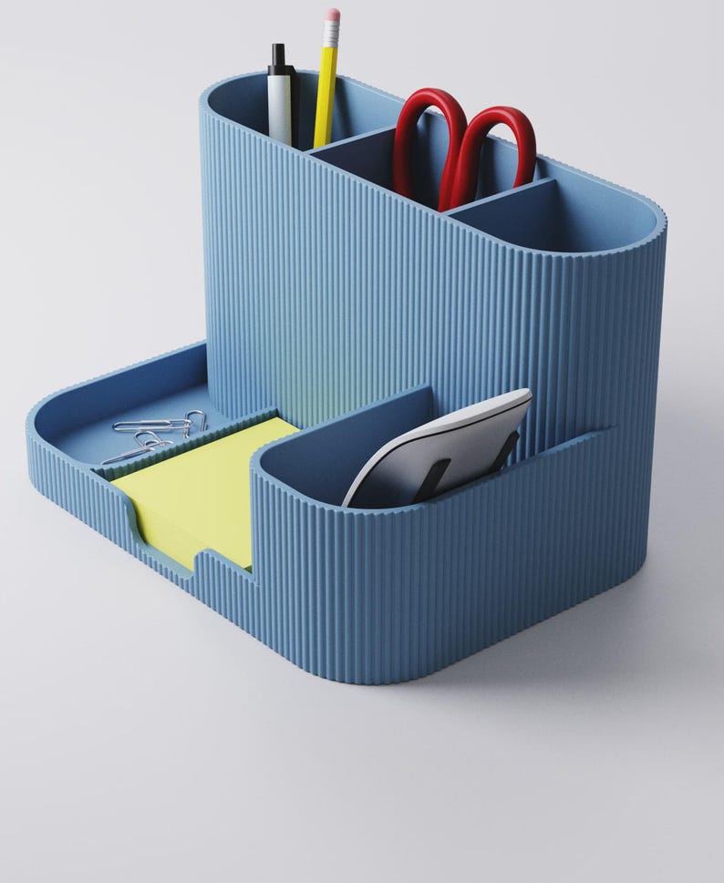 May include: A blue desk tidy with several sections. It contains a pen, pencil, and red scissors. A tray holds paper clips and yellow sticky notes. A white computer mouse is in a separate compartment.