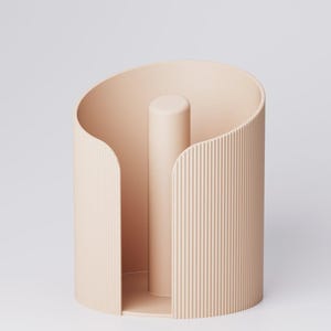 May include: A light peach-colored paper towel holder. The holder has a cylindrical shape with a central vertical post and a curved, open design. The exterior features vertical ribbed detailing, adding texture to the minimalist design.