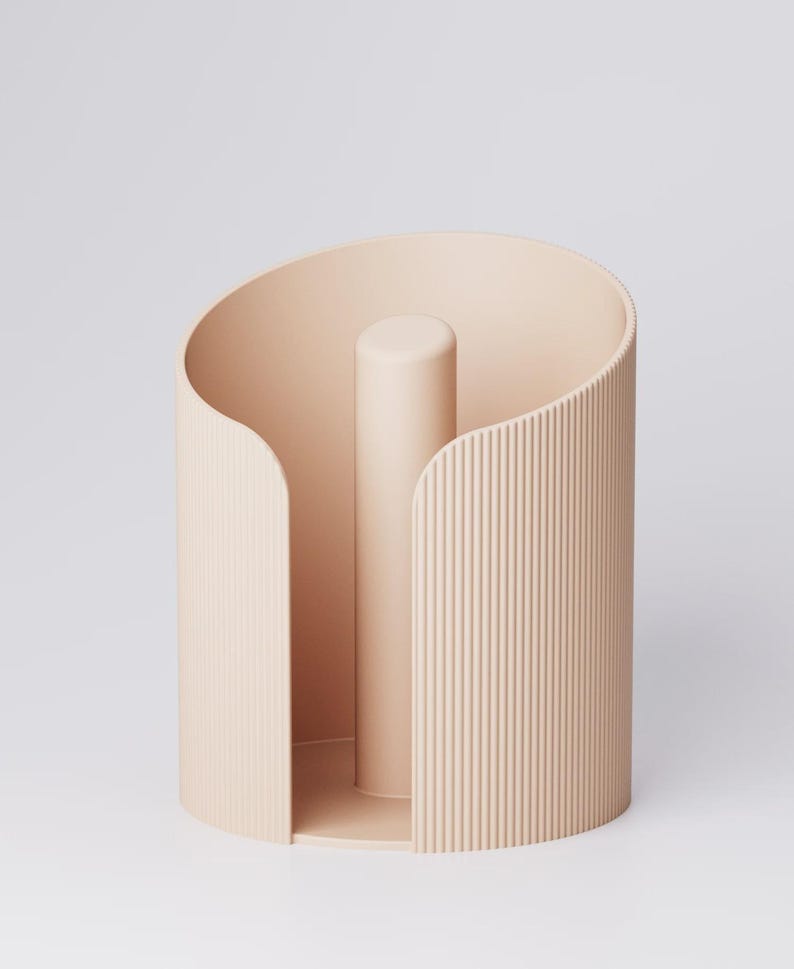 May include: A light peach-colored paper towel holder. The holder has a cylindrical shape with a central vertical post and a curved, open design. The exterior features vertical ribbed detailing, adding texture to the minimalist design.