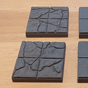 Puede incluir: Cuatro baldosas cuadradas grises texturizadas con un diseño de piedra agrietada. Las baldosas están hechas de un material plástico duro y están diseñadas para ser utilizadas como superficie de juego de mesa.