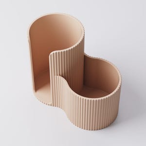 Puede incluir: Un organizador de escritorio melocot&oacute;n en forma de onda con una textura acanalada. El organizador tiene tres compartimentos de diferentes tama&ntilde;os, perfectos para guardar bol&iacute;grafos, l&aacute;pices u otros &uacute;tiles de oficina. El dise&ntilde;o es moderno y minimalista.