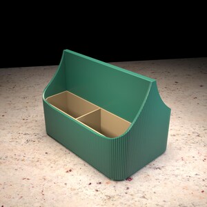 Può includere: Un organizer da scrivania color verde acqua con una texture esterna a coste e un pannello posteriore alto. L'interno è diviso in due scomparti separati con pareti color beige chiaro, offrendo uno spazio strutturato per riporre cancelleria.