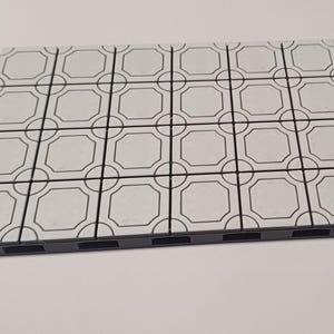 Op de afbeelding: Een witte tegel met een zwart geometrisch patroon. De tegel maakt deel uit van een grotere set tegels die kunnen worden gebruikt om een decoratieve vloer of muur te creëren.