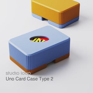 Può includere: Due custodie rettangolari per carte Uno. Una è gialla e arancione, l'altra blu e arancione, con un'apertura circolare che rivela le carte Uno. Le custodie hanno una texture a coste e sono etichettate "Uno Card Case Type 2" da "studio louo."