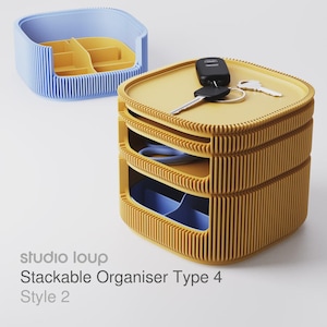 Pode incluir: Um organizador empilhável amarelo com três compartimentos, contendo chaves e um porta-chaves de carro. Um organizador azul e amarelo está no fundo. O texto "studio loup Stackable Organiser Type 4 Style 2" é visível.