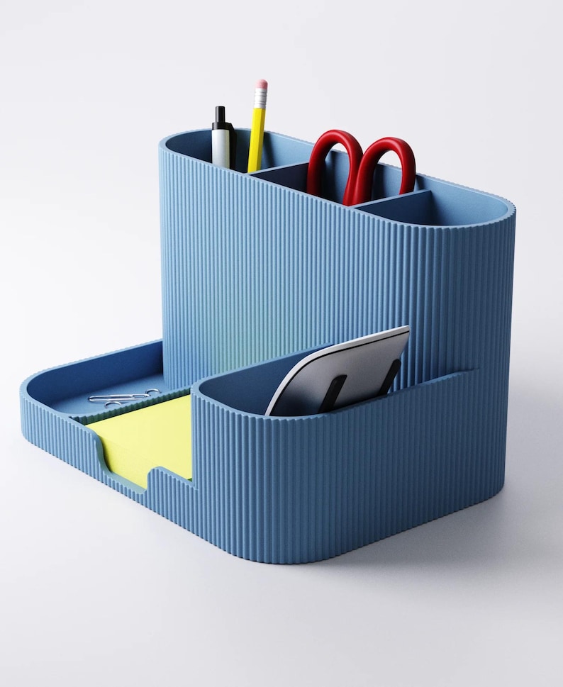 May include: A blue desk tidy with a ribbed texture. It has compartments for pens, pencils, and scissors, plus a tray for sticky notes and a slot for a tablet or phone. The organiser is a solid blue colour.