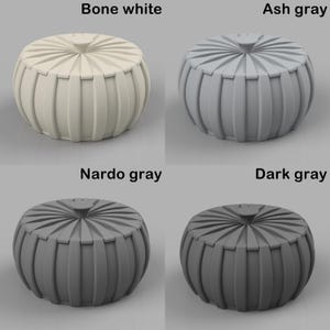 May include: Four decorative poufs in bone white, ash grey, Nardo grey, and dark grey. Each pouf has a round shape with vertical ribbed sides and a circular top with a central button. The image displays the poufs against a neutral background.