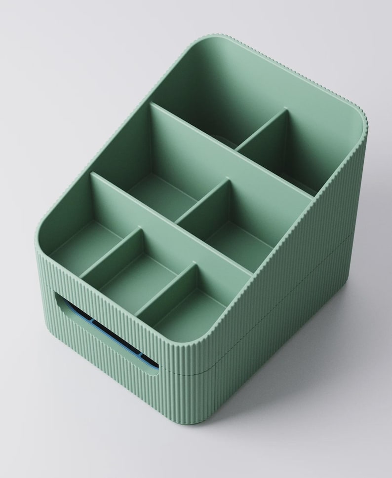 May include: A sage green organizer with multiple compartments. The rectangular container has a ribbed exterior and a handle on one side. The interior is divided into six sections, ideal for storing small items. The organizer is made of plastic.