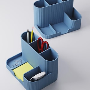 May include: Two blue desk tidies with multiple compartments. One tidy contains a pen, pencil, and red scissors. The other tidy has a notepad, paperclips, and a computer mouse. The tidies have a ribbed texture.