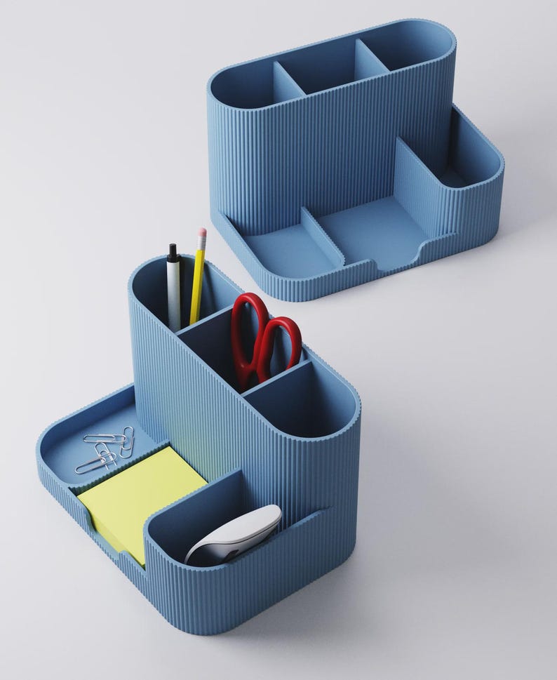 May include: Two blue desk tidies with multiple compartments. One tidy contains a pen, pencil, and red scissors. The other tidy has a notepad, paperclips, and a computer mouse. The tidies have a ribbed texture.