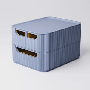 Op de afbeelding: Een opbergcontainer met twee lades in een gedempte blauwe kleur. De container heeft een geribbelde textuur aan de zijkanten en een platte bovenkant. De lade-openingen zijn rechthoekig met gele binnenkanten. Het ontwerp is modern en minimalistisch.