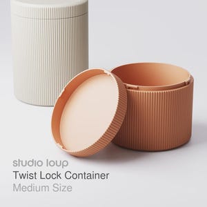 Könnte beinhalten: Drei zylindrische Behälter in neutralen Farbtönen. Die Behälter haben eine gerippte Textur und einen Drehverschluss. Der Text auf dem Bild lautet "studio loup Twist Lock Container Medium Size."