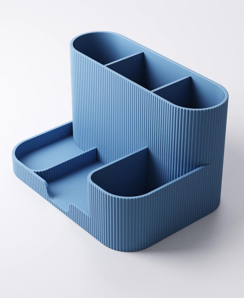 May include: A blue desk tidy with a ribbed texture. The organiser has several compartments for pens, pencils, and other stationery. It also features a small tray for holding paperclips or other small items.