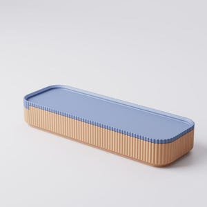 Puede incluir: Una caja de almacenamiento rectangular con tapa azul claro y base beige con estr&iacute;as verticales. La caja tiene un dise&ntilde;o limpio y moderno, adecuada para organizar objetos peque&ntilde;os. La tapa encaja a ras con la base.