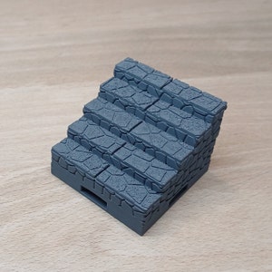 Op de afbeelding: Een grijze stenen trapminiaturen, perfect voor tabletop gaming of miniaturen dioramas. De trap is gemaakt van getextureerd plastic en heeft een realistische stenen uitstraling.