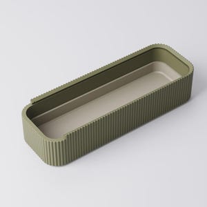 Peut inclure: Un plateau de rangement rectangulaire vert olive avec un ext&eacute;rieur nervur&eacute; et un int&eacute;rieur beige clair. Le plateau a des coins arrondis et un design minimaliste. L'int&eacute;rieur pr&eacute;sente une section l&eacute;g&egrave;rement sur&eacute;lev&eacute;e. Le plateau est vide et repose sur une surface blanche.