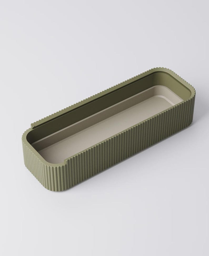 Peut inclure: Un plateau de rangement rectangulaire vert olive avec un ext&eacute;rieur nervur&eacute; et un int&eacute;rieur beige clair. Le plateau a des coins arrondis et un design minimaliste. L'int&eacute;rieur pr&eacute;sente une section l&eacute;g&egrave;rement sur&eacute;lev&eacute;e. Le plateau est vide et repose sur une surface blanche.