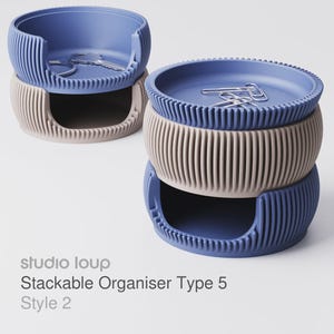 Op de afbeelding: Stapelbare organizer set in blauw en beige. De organizers hebben een geribbeld ontwerp en een cirkelvorm. Het bovenste gedeelte is blauw en het onderste gedeelte is beige. De set bevat paperclips en sleutels. De tekst op de afbeelding luidt "studio loup Stackable Organiser Type 5 Style 2".