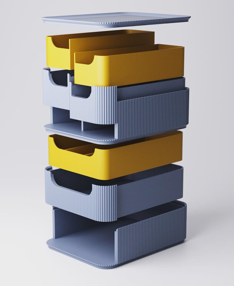 Op de afbeelding: Een stapelbare opbergorganizer met een deksel. De organizer heeft afwisselend gele en blauwgrijze lades. De lades hebben een geribbeld ontwerp aan de voorkant en een uitsparing voor een gebogen handgreep. Het deksel en de basis zijn ook blauwgrijs.