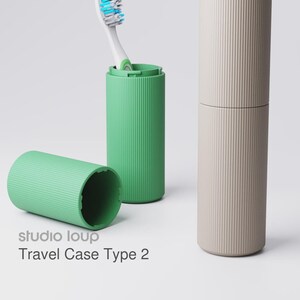May include: A green travel toothbrush case with a toothbrush inside, a separate green lid, and a beige travel case. The cases have vertical ribbed detailing. The text "studio loup Travel Case Type 2" is visible.