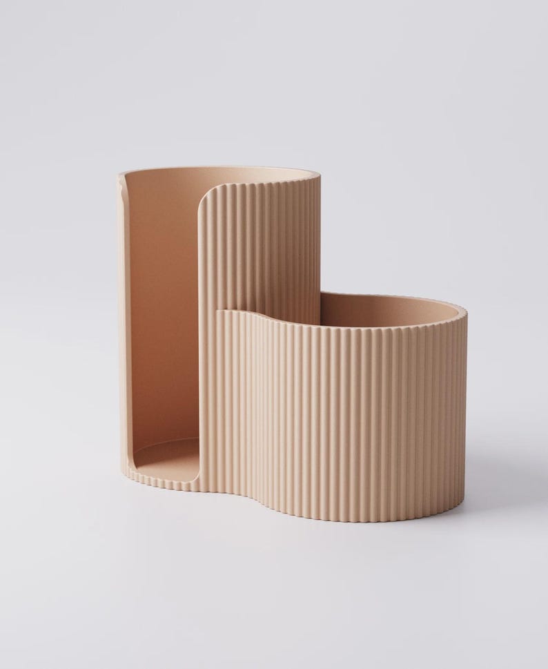 Puede incluir: Un organizador de escritorio beige moderno con un dise&ntilde;o ondulado &uacute;nico. El organizador tiene una secci&oacute;n alta y abierta y una secci&oacute;n m&aacute;s corta y curva, ambas con detalles acanalados verticales. El color neutro y el estilo minimalista son adecuados para cualquier decoraci&oacute;n.