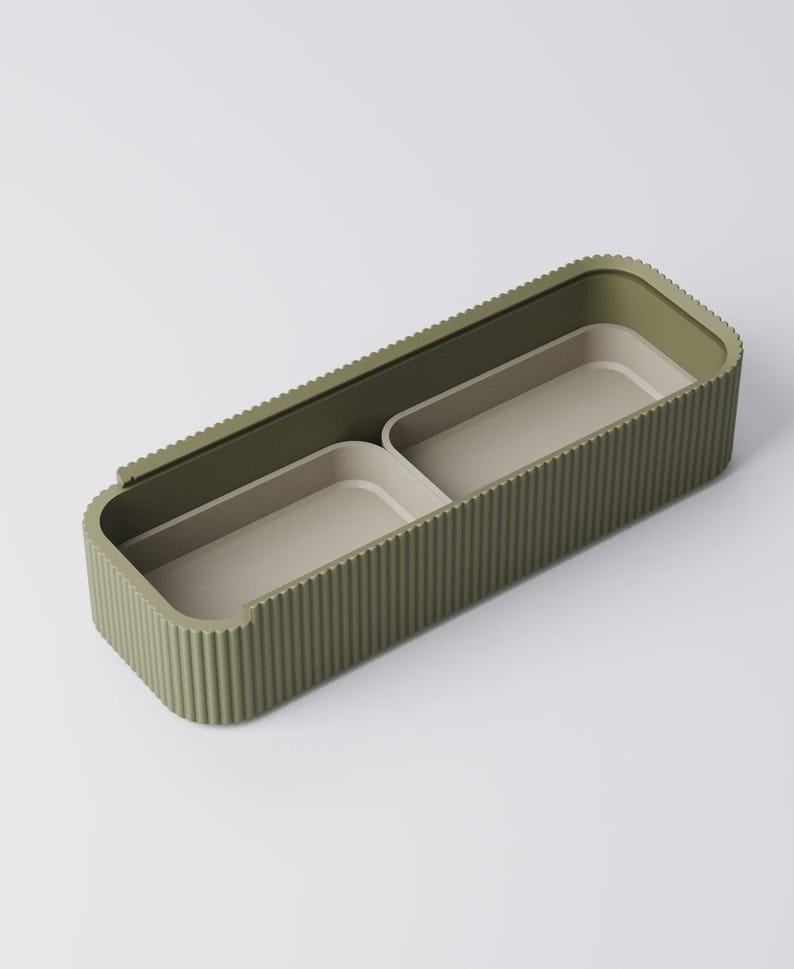 Peut inclure: Un conteneur de rangement rectangulaire vert olive avec un ext&eacute;rieur nervur&eacute; et deux compartiments int&eacute;rieurs. Les compartiments int&eacute;rieurs sont de couleur beige clair. Le conteneur est con&ccedil;u pour organiser de petits objets.