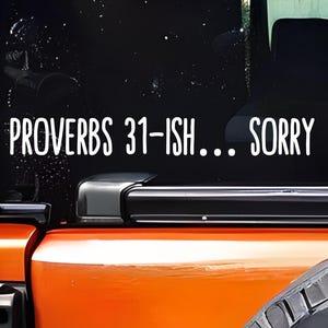 May include: White vinyl decal applied to a vehicle's rear window. The text reads "PROVERBS 31-ISH... SORRY" in a bold, sans-serif font. The vehicle is orange and black.