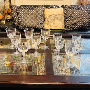 May include: A collection of clear crystal wine glasses with intricate cut patterns. The glasses are arranged on a mirrored surface, reflecting the light and creating a sparkling display. The stemware is elegant and suitable for formal occasions.