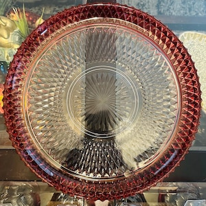 Op de afbeelding: Een grote, heldere glazen serveerschaal met een dieprode rand en een diamantpatroon. De schaal heeft een verhoogd midden met een stervormig ontwerp.