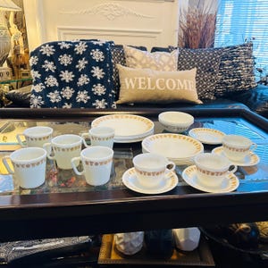 Könnte beinhalten: Ein Set aus weißem und goldenem Vintage-Geschirr von Corelle mit einem Blumenmuster. Das Set enthält Teller, Schalen und Tassen.