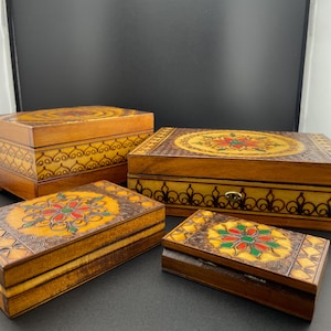 Könnte beinhalten: Satz von vier Holzkisten mit aufwendigen floralen Designs, die in Rot, Grün und Gelb bemalt sind. Die Kisten sind ineinander verschachtelt, wobei die größte Kiste unten und die kleinste oben liegt.