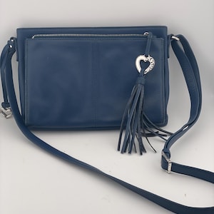 May include: A navy blue crossbody bag with a front pocket and a silver zipper. The bag features a silver heart-shaped charm with a tassel. The adjustable strap is also navy blue.