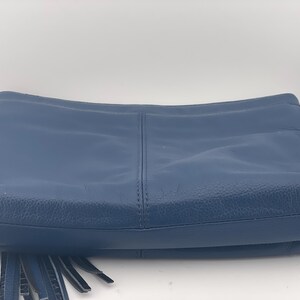 May include: A navy blue leather crossbody bag with a long adjustable strap and silver-tone hardware. The bag features a front flap with fringe detailing and a stitched center seam. The bag is designed for everyday use.