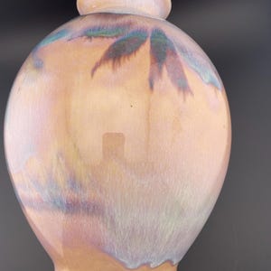 May include: A pearlescent ceramic vase with a rounded body and a narrow neck. The vase has a glossy finish with iridescent hues of peach, blue, and green. The design features a subtle leaf-like pattern near the top.