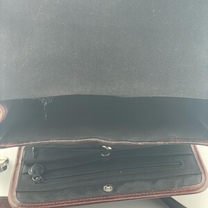 May include: Open view of a brown leather crossbody bag with a textured strap and silver buckle. The bag's interior is black, with a zippered pocket and a magnetic closure on the flap.