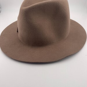 Puede incluir: Un sombrero fedora marr&oacute;n con ala ancha. El sombrero tiene una corona cl&aacute;sica en forma de l&aacute;grima y una cinta de grogr&eacute;n. El sombrero est&aacute; hecho de un material suave similar al fieltro y es adecuado para varias ocasiones.