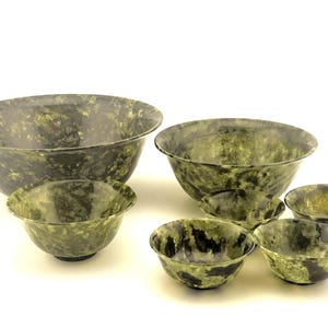 Puede incluir: Un conjunto de seis cuencos con un patrón moteado verde y negro. Los cuencos, de diferentes tamaños, presentan una superficie lisa y una forma redondeada. El cuenco más grande mide unos 30 cm de diámetro, ideal para servir o decorar.