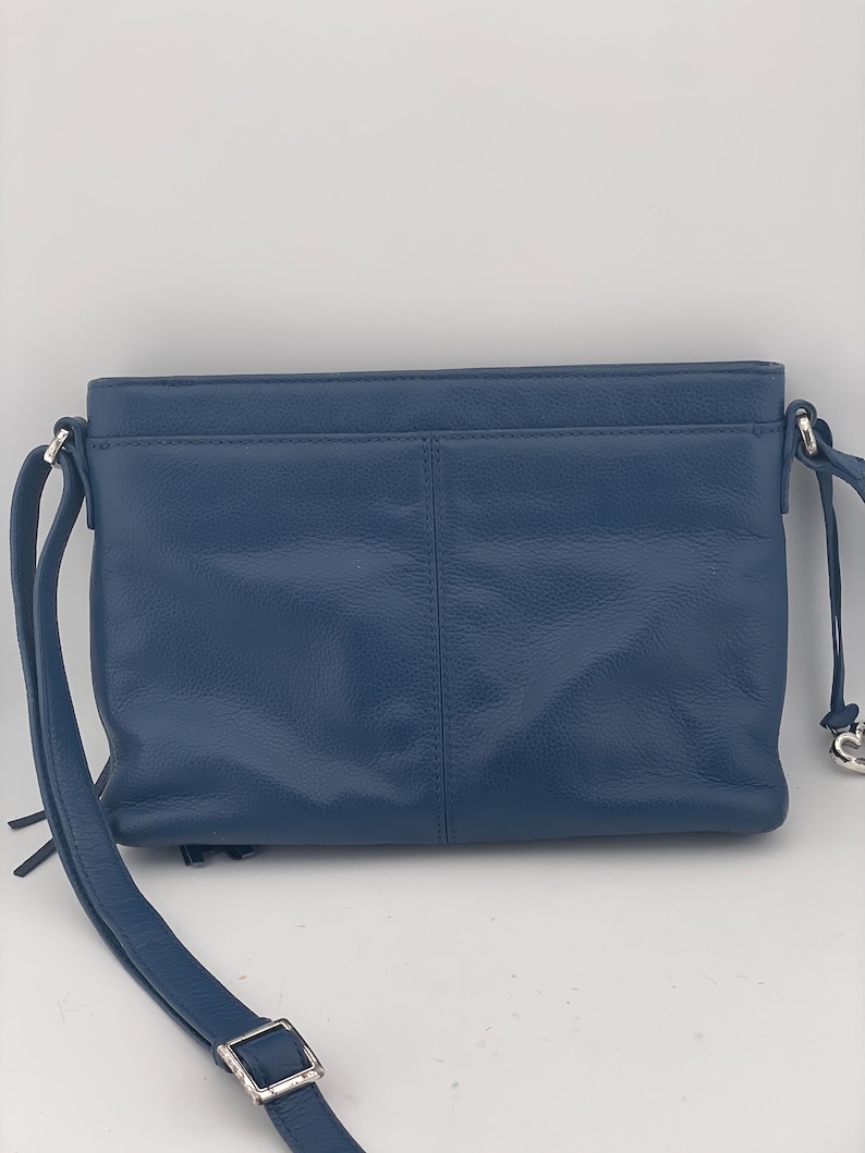 May include: A blue leather crossbody bag with a long adjustable strap and silver-toned hardware. The bag has a rectangular shape with a front pocket and a top zipper closure. The bag's strap is 48 inches long.