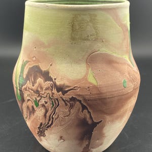 Pode incluir: Um vaso de cerâmica com um design marmorizado em tons de marrom, verde e branco. O vaso tem uma forma arredondada e uma borda ligeiramente alargada.