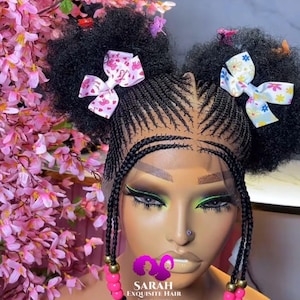 May include: A black wig with braided hair styled in two buns with pink and white bows. The wig has beaded strands hanging down the sides. The wig is on a mannequin head with makeup.