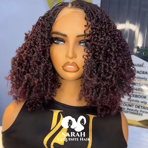 Può includere: Parrucca riccia bordeaux scuro su una testa di manichino. La parrucca presenta un'attaccatura dei capelli intrecciata e uno stile corto e voluminoso. Il manichino indossa un top nero con il logo dorato "SARAH EXQUISITE HAIR".