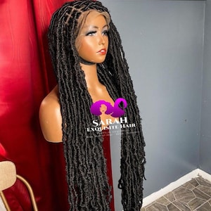 Può includere: Una parrucca nera in crochet con pizzo frontale e lunghi dreadlocks sciolti. La parrucca è acconciata con una riga laterale e ha una texture naturale e ondulata. La parrucca è su una testa di manichino e si trova su uno sfondo rosso.