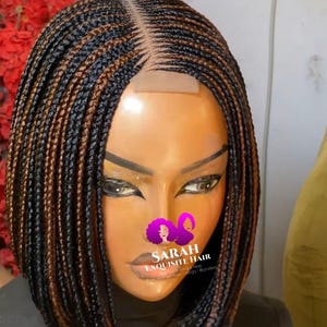 May include: A brown and black braided wig with a lace front. The wig is styled in a bob with the braids extending past the shoulders. The wig is on a mannequin head.