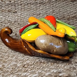 May include: A ceramic cornucopia overflowing with colourful, glazed vegetables. The arrangement includes a potato, tomatoes, peppers, and squash in shades of red, green, yellow, and orange. The cornucopia is brown.