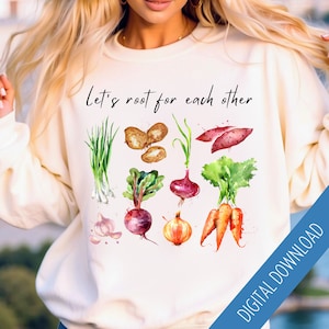 May include: White sweatshirt with the text "Let's root for each other" in black lettering. The sweatshirt features a watercolor illustration of various root vegetables, including onions, potatoes, carrots, beets, and garlic.