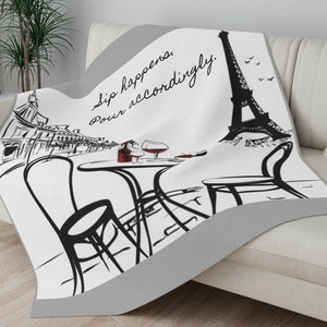 May include: White and gray throw blanket with a black and white illustration of the Eiffel Tower, a Parisian cafe scene, and the text "Sip happens. Pour accordingly."